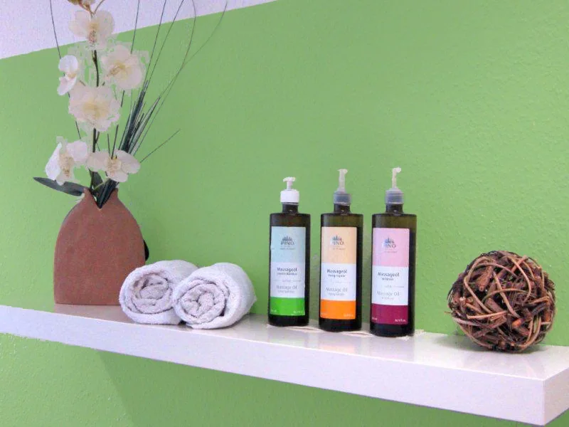 Regal mit Massageölen, Handtüchern und Orchidee vor grüner Wand